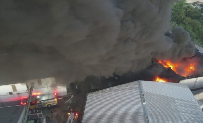 Bomberos y drones del 911 siguen combatiendo fuego en empresa de plásticos en Haina